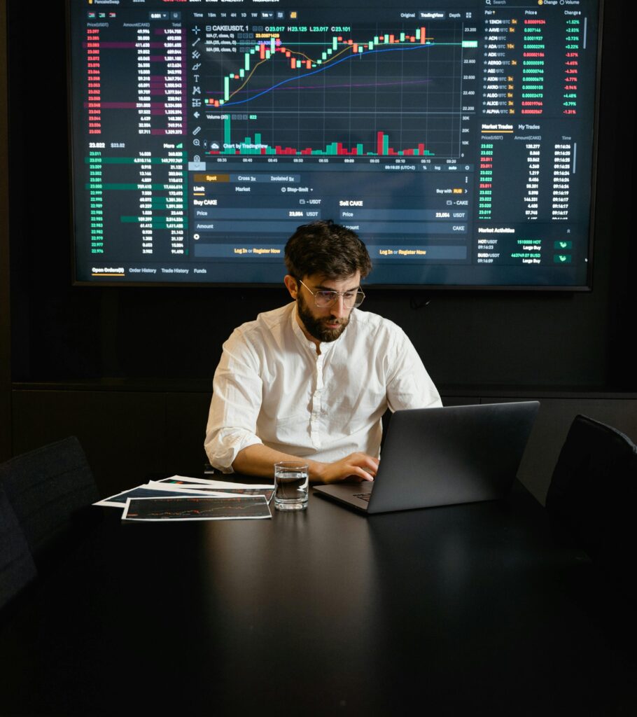 pexels-photo-7567529-7567529 A focused man analyzing stock market trends on a laptop in an office setting with charts displayed.