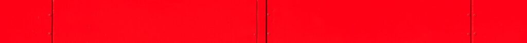 pexels-photo-33537964-33537964 Close-up of a vibrant red industrial wall with geometric panel design and small openings.